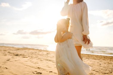 Kumsalda kızıyla birlikte gün batımında birlikte eğlenen mutlu anne portresi. Genç bir kadın ve küçük bir kız gülüyor ve deniz manzarasının tadını çıkarıyor. Çocukluk, annelik kavramı..