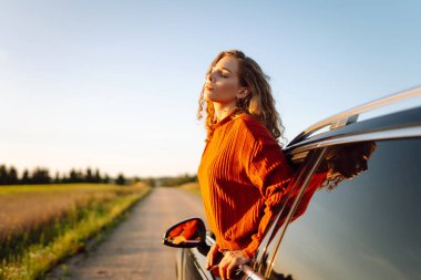 Mutlu kadın arabanın camından sarkıyor ve pencereden manzaranın tadını çıkarıyor. Genç bayan gezgin yol macerasında özgürlüğü hissediyor. Seyahat, özgürlük konsepti. Etkin yaşam biçimi.