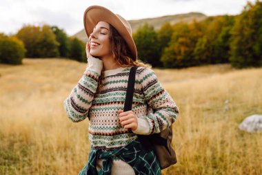 Elinde evrak çantasıyla dağ yolunda doğa ile eğlenen genç bir kadın yürüyüşçü. Yürüyüşe çıkmış gezgin ve açık havada özgürlüğü hissediyor. Yürüyüş, seyahat ve doğa konsepti. Etkin yaşam biçimi.