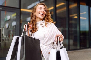 Modern bir alışveriş merkezinin girişinde alışveriş torbaları olan mutlu bir kadın. Genç bir kadın dışarıda eğleniyor. Tüketim konsepti, indirimler, alışveriş.