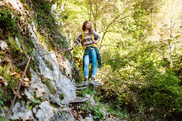 Sırt çantalı gülümseyen bir kadın sık güneşli ormanda kayalık yolda yürüyor. Genç bayan yürüyüşçü dağlık alanda yürüyüş yapıyor. Özgürlük, macera ve doğa kavramı.