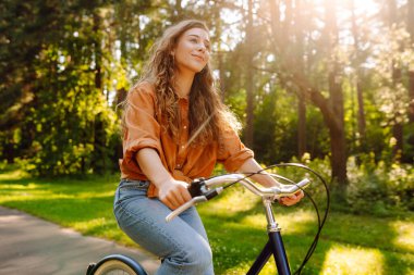 Güneşli bir parkta bisiklet süren mutlu bir kadın. Doğanın tadını çıkaran, dışarıda eğlenen genç bir kadın. Boş zaman, hafta sonu ve özgürlük konsepti. Etkin yaşam biçimi.
