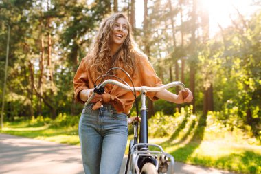 Güneşli bir parkta bisiklet süren mutlu bir kadın. Doğanın tadını çıkaran, dışarıda eğlenen genç bir kadın. Boş zaman, hafta sonu ve özgürlük konsepti. Etkin yaşam biçimi.