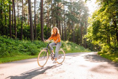 Güneşli bir parkta bisiklet süren mutlu bir kadın. Doğanın tadını çıkaran, dışarıda eğlenen genç bir kadın. Boş zaman, hafta sonu ve özgürlük konsepti. Etkin yaşam biçimi.