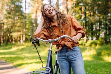 Güneşli bir parkta bisiklet süren mutlu bir kadın. Doğanın tadını çıkaran, dışarıda eğlenen genç bir kadın. Boş zaman, hafta sonu ve özgürlük konsepti. Etkin yaşam biçimi.