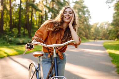 Güneşli bir parkta bisiklet süren mutlu bir kadın. Doğanın tadını çıkaran, dışarıda eğlenen genç bir kadın. Boş zaman, hafta sonu ve özgürlük konsepti. Etkin yaşam biçimi.