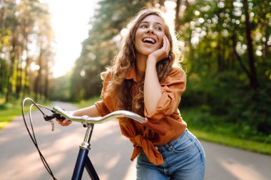 Güneşli bir parkta bisiklet süren mutlu bir kadın. Doğanın tadını çıkaran, dışarıda eğlenen genç bir kadın. Boş zaman, hafta sonu ve özgürlük konsepti. Etkin yaşam biçimi.