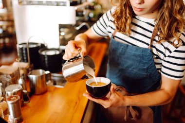Önlüklü bir barmen barın arkasında kahve makinesiyle kahve hazırlar. Deneyimli bir barista sütünü köpürtür ve sıcak bir kafede taze espresso hazırlar. Tüketim konsepti, yemek servisi..