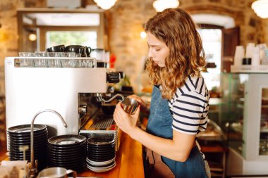 Önlüklü bir barmen barın arkasında kahve makinesiyle kahve hazırlar. Deneyimli bir barista sütünü köpürtür ve sıcak bir kafede taze espresso hazırlar. Tüketim konsepti, yemek servisi..