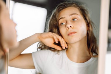 İsilik olmuş, rahat bir odada aynaya bakan genç bir kadının yakın plan yüzü. Derisi sorunlu güzel bir kadın doğal güzelliğinin tadını çıkarıyor. Dermatoloji konsepti, güzellik ve doğallık.