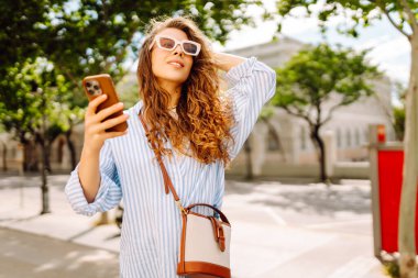 Telefonu olan genç bir turist selfie çekiyor ve güneşli caddelerde blog yazıyor. Dışarıda gezmekten hoşlanan güzel bir kadın. Blogculuk, turizm konsepti.