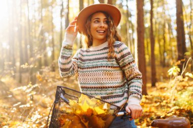 Parlak yapraklarla çevrili güz güneşli bir ormanda bisiklet süren neşeli bir kadın. Şapkalı genç bir kadın eğleniyor ve dışarıda bisikletle dolaşıyor. Eğlence konsepti, eğlence.