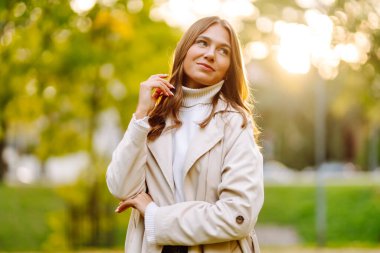 Gündelik giysiler içinde güzel bir kadın sonbahar parkında yürüyor ve güneşli havanın tadını çıkarıyor. Açık havada poz veren hoş bir kadın. Güzellik ve hafta sonu konsepti. Yaşam biçimi.