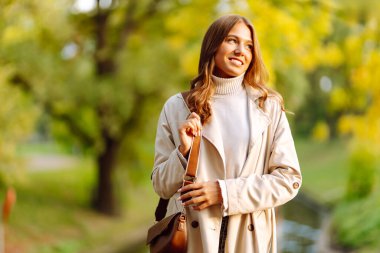 Gündelik giysiler içinde güzel bir kadın sonbahar parkında yürüyor ve güneşli havanın tadını çıkarıyor. Açık havada poz veren hoş bir kadın. Güzellik ve hafta sonu konsepti. Yaşam biçimi.