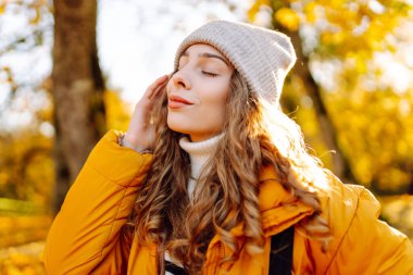 Parlak ceketli şirin bir kadın sarı sonbahar parkında yürüyor. Sırt çantalı genç bir turist güneşli bir günün ve sonbaharın tadını çıkarıyor. Doğa, eğlence konsepti.