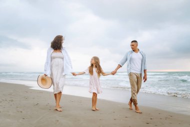 Kumsalda el ele tutuşarak yürüyen mutlu bir aile. Hamile karısı ve kızıyla birlikte dışarıda özgürce vakit geçiren bir adam. Aile, hafta sonu konsepti.