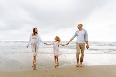 Kumsalda el ele tutuşarak yürüyen mutlu bir aile. Hamile karısı ve kızıyla birlikte dışarıda özgürce vakit geçiren bir adam. Aile, hafta sonu konsepti.