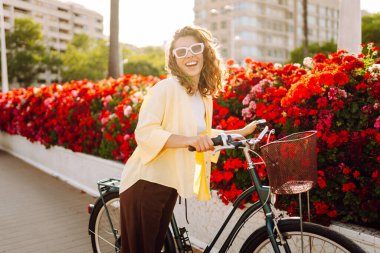 Şık kıyafetler içinde neşeli bir kadın güneşli bir şehirde bisiklet sürüyor. Turist zevk alır ve dışarıda bisikletle vakit geçirir. Turizm konsepti. Yaşam biçimi.