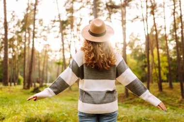 Yoğun bir ormanda, güneş ışınları altında neşeli bir kadının portresi. Parkta yürüyüş yapan güzel bir kadın. Hafta sonu ve eğlence konsepti. Etkin yaşam biçimi.