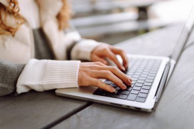 Bilgisayarlı genç bir kadın parkta bir masada oturmuş, doğanın tadını çıkarıyor. Dışarıda dizüstü bilgisayarda çalışan serbest çalışan bir kadın. Uzak çalışma ve teknoloji kavramı.