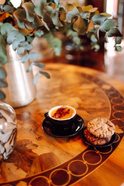 Bir fincan aromatik kapuçinonun kapuçinosunun yakın çekimi güneş batarken ahşap bir masanın üzerinde duruyor. Kahve dükkanında tatlı ile nefis bir sıcak içecek. Yiyecek ve içecek konsepti.