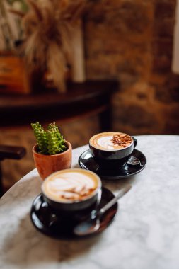 Bir fincan aromatik kapuçinonun kapuçinosunun yakın çekimi güneş batarken ahşap bir masanın üzerinde duruyor. Kahve dükkanında tatlı ile nefis bir sıcak içecek. Yiyecek ve içecek konsepti.