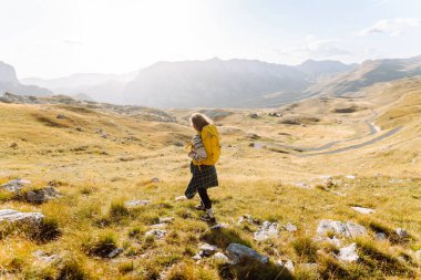 Renkli sırt çantalı kadın yürüyüşçü görkemli dağların arasında özgürlüğünü hissediyor. Genç bayan gezgin dağ manzarasının tadını çıkarıyor. Doğa ve özgürlük kavramı.