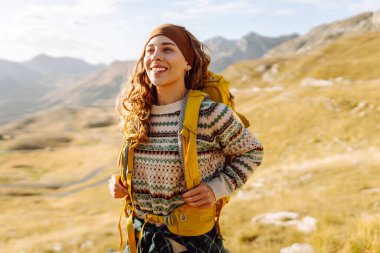 Renkli sırt çantalı kadın yürüyüşçü görkemli dağların arasında özgürlüğünü hissediyor. Genç bayan gezgin dağ manzarasının tadını çıkarıyor. Doğa ve özgürlük kavramı.
