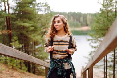 Sırt çantalı genç bir yürüyüşçü. Yürüyen ahşap bir patikada, göle bakan. Kadın gezgin ormanda doğanın tadını çıkarıyor ve özgürlüğü hissediyor. Macera konsepti.