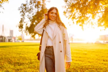 Genç bir kadın güneşli bir parkta duruyor ve yürümekten hoşlanıyor. Şık giyinmiş güzel bir kadın dışarıda dinleniyor. Yürüyüş, güzellik ve moda konsepti.