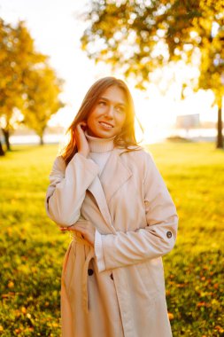 Genç bir kadın güneşli bir parkta duruyor ve yürümekten hoşlanıyor. Şık giyinmiş güzel bir kadın dışarıda dinleniyor. Yürüyüş, güzellik ve moda konsepti.