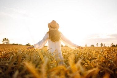 Beyaz elbiseli ve hasır şapkalı bir kadının altın buğday tarlasında dikiz aynasından görünüşü. Güzel bir kadın gün batımından zevk alır ve açık havada özgür hisseder. Güzellik kavramı, özgürlük, takip et.