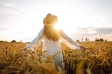 Beyaz elbiseli ve hasır şapkalı bir kadının altın buğday tarlasında dikiz aynasından görünüşü. Güzel bir kadın gün batımından zevk alır ve açık havada özgür hisseder. Güzellik kavramı, özgürlük, takip et.