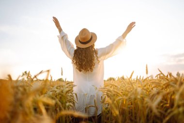 Beyaz elbiseli ve hasır şapkalı bir kadının altın buğday tarlasında dikiz aynasından görünüşü. Güzel bir kadın gün batımından zevk alır ve açık havada özgür hisseder. Güzellik kavramı, özgürlük, takip et.