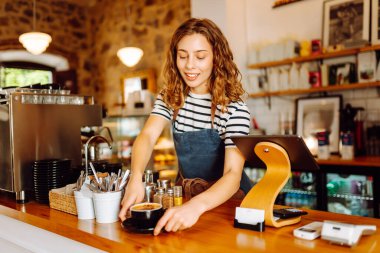 Genç bir bayan barmen hazır kahveyle bir barın arkasında duruyor. Dijital tabletli güzel bir kadın sıcak bir kahve dükkanında güneş ışığının tadını çıkarıyor. Küçük işletme, içecek konsepti.