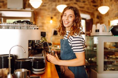 Genç bir bayan barmen hazır kahveyle bir barın arkasında duruyor. Dijital tabletli güzel bir kadın sıcak bir kahve dükkanında güneş ışığının tadını çıkarıyor. Küçük işletme, içecek konsepti.