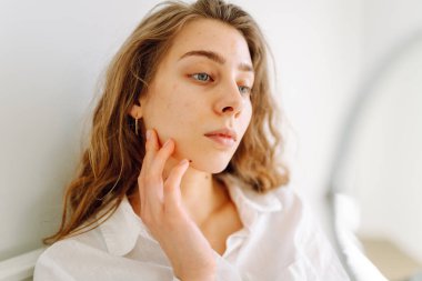 Samimi bir odada küçük bir aynaya bakan genç bir kadının portresi. Güzel bir kadın elleriyle yüzüne dokunur ve doğal güzellikten zevk alır. Güzellik kavramı, dermatoloji, rahatlık.