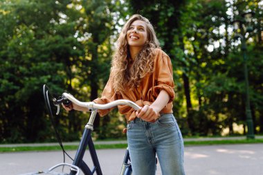 Güneşli bir parkta bisikleti olan neşeli bir kadın. Doğanın tadını çıkaran ve gün batımında bisiklete binen güzel bir kadın. Eğlence kavramı, yürü. Yaşam biçimi.