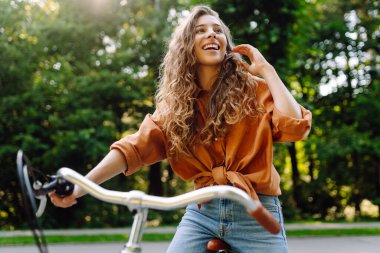 Güneşli bir parkta bisikleti olan neşeli bir kadın. Doğanın tadını çıkaran ve gün batımında bisiklete binen güzel bir kadın. Eğlence kavramı, yürü. Yaşam biçimi.