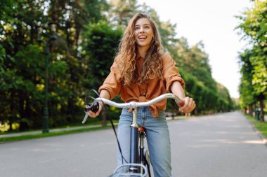 Güneşli bir parkta bisikleti olan neşeli bir kadın. Doğanın tadını çıkaran ve gün batımında bisiklete binen güzel bir kadın. Eğlence kavramı, yürü. Yaşam biçimi.