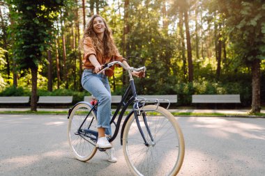 Güneşli bir parkta bisikleti olan neşeli bir kadın. Doğanın tadını çıkaran ve gün batımında bisiklete binen güzel bir kadın. Eğlence kavramı, yürü. Yaşam biçimi.