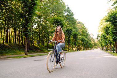 Güneşli bir parkta bisikleti olan neşeli bir kadın. Doğanın tadını çıkaran ve gün batımında bisiklete binen güzel bir kadın. Eğlence kavramı, yürü. Yaşam biçimi.