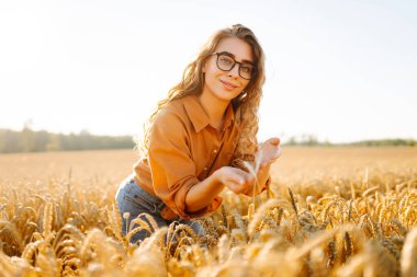 Tarım alanında altın buğday saplarını ayıran şapkalı ve gözlüklü kadın tarımcı. Genç kadın çiftçi buğday hasadının kalitesini kontrol ediyor. Çiftçilik kavramı, zengin hasat.