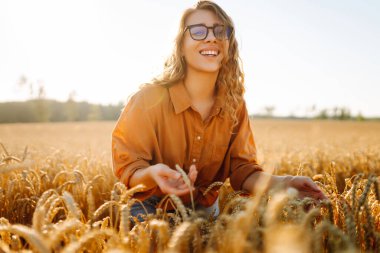 Tarım alanında altın buğday saplarını ayıran şapkalı ve gözlüklü kadın tarımcı. Genç kadın çiftçi buğday hasadının kalitesini kontrol ediyor. Çiftçilik kavramı, zengin hasat.