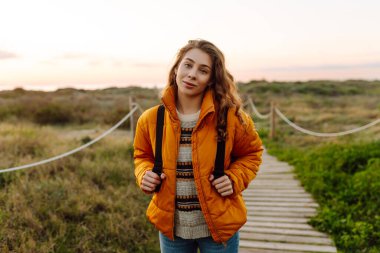 Sırt çantalı kadın yürüyüşçü deniz manzarasına karşı yürüyen ahşap yolda. Mutlu kadın gün batımında yürüyor ve maceranın tadını çıkarıyor. Yürüyüş konsepti. Etkin yaşam biçimi.