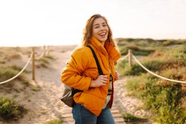 Sırt çantalı kadın yürüyüşçü deniz manzarasına karşı yürüyen ahşap yolda. Mutlu kadın gün batımında yürüyor ve maceranın tadını çıkarıyor. Yürüyüş konsepti. Etkin yaşam biçimi.