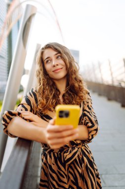 Gün batımında köprüde telefonu olan neşeli bir kadın. Genç turist akıllı telefondan blog yazıyor ve havanın tadını çıkarıyor. Blogculuk, turizm ve teknoloji kavramı.