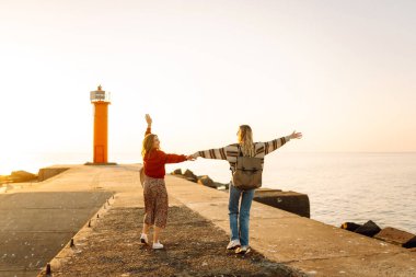 İki bayan arkadaş deniz fenerinin arka planında eğleniyor ve rıhtımda yürüyorlar. Güzel kadınlar gün batımını ve birlikte dışarıda vakit geçirmeyi seviyorlar. Arkadaşlık kavramı, yürüme.