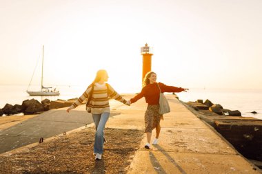 İki bayan arkadaş deniz fenerinin arka planında eğleniyor ve rıhtımda yürüyorlar. Güzel kadınlar gün batımını ve birlikte dışarıda vakit geçirmeyi seviyorlar. Arkadaşlık kavramı, yürüme.