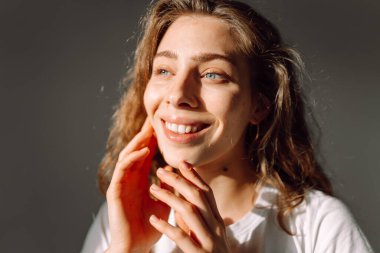 Sıcak bir odada otururken yüzüne dokunan sevimli bir kadının portresi. Güneş ışınlarının ve doğal güzelliğin tadını çıkaran güzel bir kadın. Doğal güzellik, dermatoloji ve kozmetoloji kavramı.